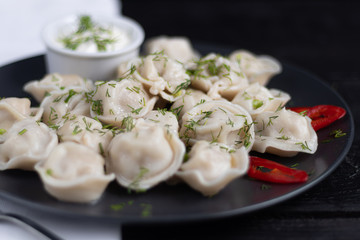 Boiled dumplings. In the background are greens, red peppers and bay leaves. On a black wooden background with a white napkin.