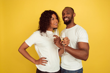 Drinking champagne. Valentine's day celebration, happy african-american couple isolated on yellow studio background. Concept of human emotions, facial expression, love, relations, romantic holidays.