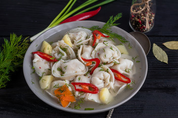 Soup with dumplings. In the background are greens, red peppers and bay leaves. On a black wooden background. Copy space.