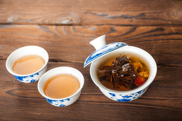 Knitted blooming tea in a porcelain teapot close-up. Tea ceremony on a dark wooden background and copy space.