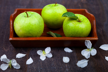 Green apples, flowers and leaves on a wooden tray.