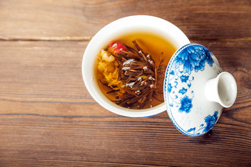 Knitted blooming tea in a porcelain teapot close-up. Tea ceremony on a dark wooden background and...