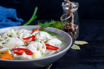 Soup with dumplings. In the background are greens, red peppers and bay leaves. On a black wooden background. Copy space.