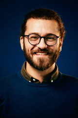 Obraz premium Portret całkiem uśmiechnięty brodaty hipster przed niebieskim tle i patrząc na kamery.