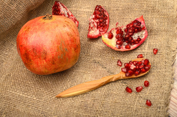Ripe juicy pomegranate, pieces of pomegranate and pomegranate seeds on a wooden spoon on a background of rough homespun fabric. Close up.