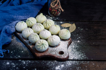Frozen khinkali on a wooden board, sprinkled with flour. In the background pepper and bay leaf. On a black wooden background.