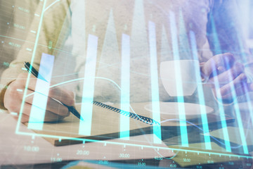 Forex chart hologram on hand taking notes background. Concept of analysis. Double exposure