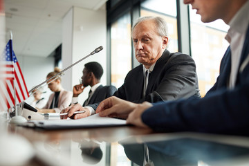 Serious senior businessman sitting and examining the report during press conference