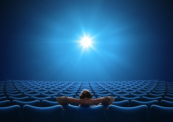 Empty blue cinema with VIP sitting in center and looking on bright screen. Mixed media.