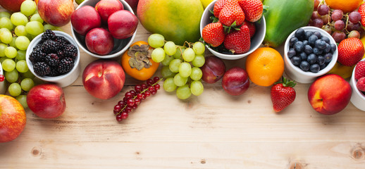 Healthy colorful fruits berries, strawberries oranges plums grapes mango papaya red currants peaches on wooden table, top view, copy space, selective focus - obrazy, fototapety, plakaty