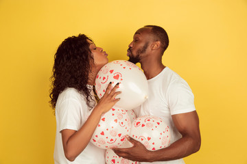 Holding balloons. Valentine's day celebration, happy african-american couple isolated on yellow studio background. Concept of human emotions, facial expression, love, relations, romantic holidays.