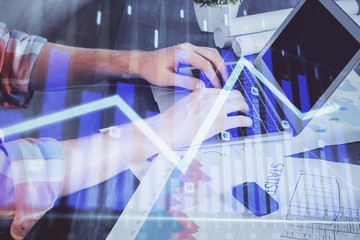 Double exposure of stock graph with businessman typing on computer in office on background. Concept of hard work.