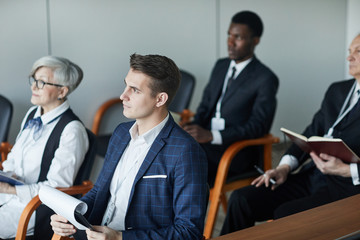 Group of business people sitting on chairs with documents and listening to the speaker during seminar
