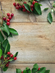 Fresh sweet cherries with leaves on wooden background, top view.