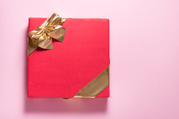 Red gift box with gold ribbon on pink background, copy space