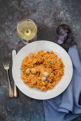 rice with seafood on white plate and glass of white wine