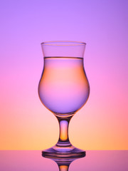  glass for cocktail with water on a colored background, with reflection,.sunset color, purple; pink; orange;