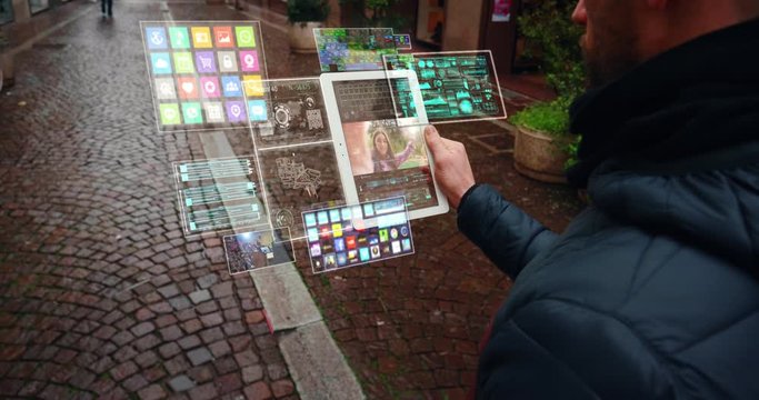 Close up of an young man is making a video call to his girlfriend with a futuristic latest innovative technology glass tablet with augmented reality holograms during walking in city center by day.