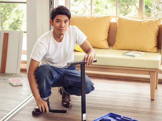  Asian man trying to assemble knockdown furniture and getting confused. - obrazy, fototapety, plakaty