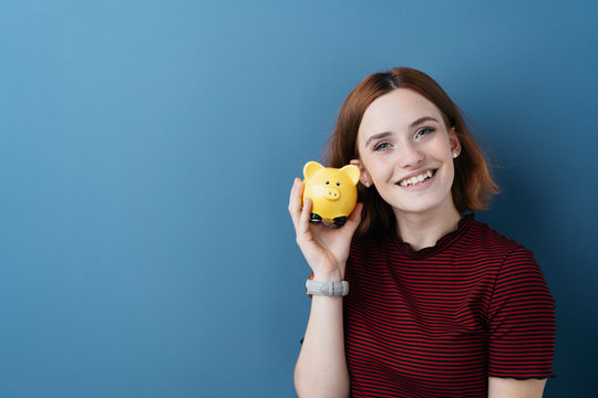 Happy young woman holding a yellow piggy bank