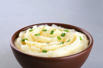 Bowl with mashed potatoes and onions on gray texture.