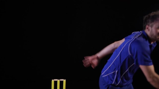 Cricket Bowler bowling the ball in a game of the sport- Black background. Dressed in blue. TwentyTwenty - Stock 4K Video Clip Footage