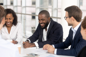 Smiling diverse employees laugh brainstorming at office meeting