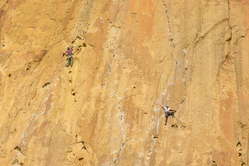 Climbers climb a large rock, filmed from the back. With space