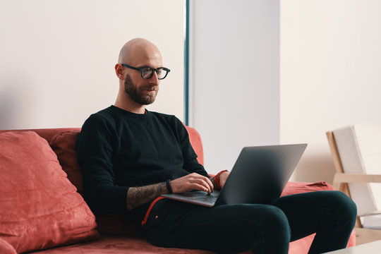 Modern young caucasian man with beard and glasses relaxing while surfing internet on laptop pc