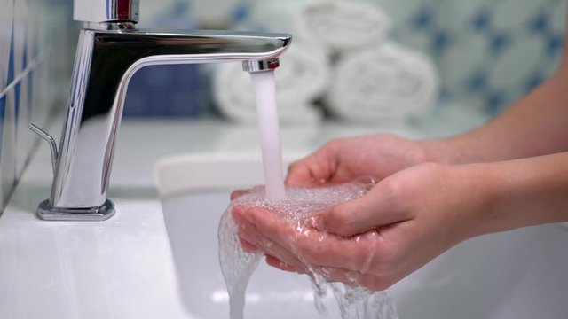 Slow motion shot of water running over hands in sink