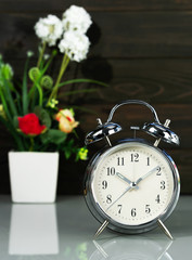 Alarm clock and flower vase on table