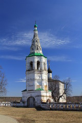 White stone bell tower of an old Church against the blue sky and yellow field