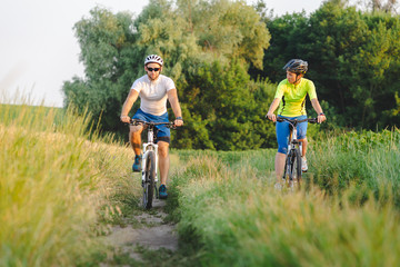 young man and woman ride bicycles between fields in summer.
