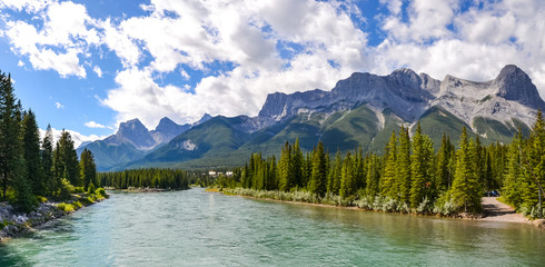 The mountain range spreads across the view just as the pine forest spreads across the landscape from the rivers edge up to the rocky mountainsides on this sunny, partially cloudy day.