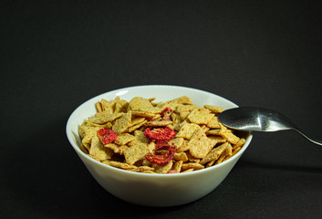 Dry Strawberry Diet Wheat Cereal Bowl with Spoon on Black Background