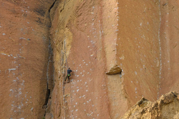 Rock climbers climb a large rock, filmed from the back.