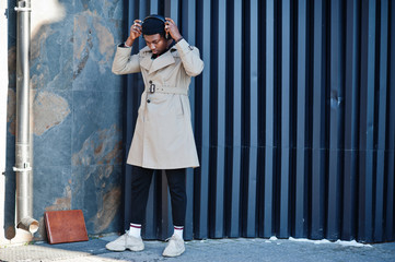 African american man with headphones, wear on hat and coat listening music on steel background.