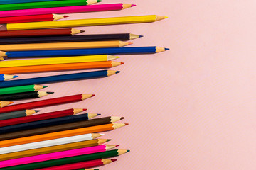 Scattered colored pencils of different lengths on a pink background on the left side, tending to the center. Horizontal close-up