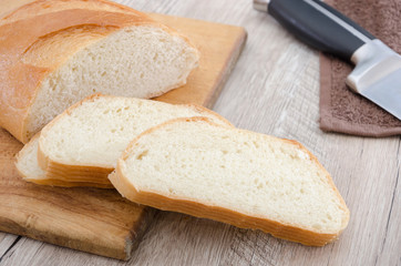 long loaf on a wooden board and knife. Delicious Ukrainian bread. Sliced white bread.