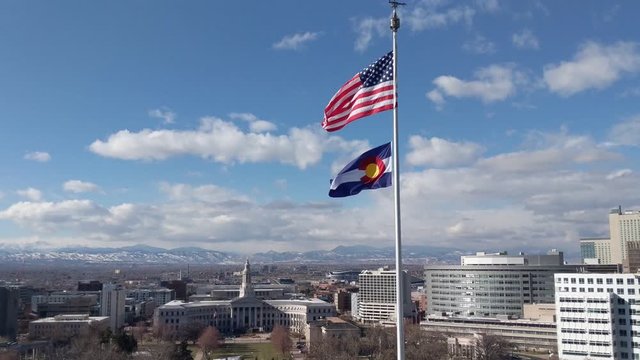 View of the American Flag and the Colorado state flag blowing in the slight breeze looking west towards the Rocky Mountains from downtown Denver.