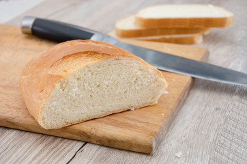 long loaf on a wooden board and knife. Delicious Ukrainian bread. Sliced white bread.