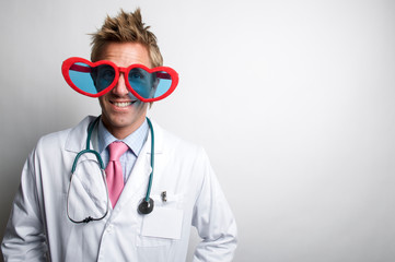 Love Doctor wearing white lab coat and stethoscope smiling behind big red heart-shaped glasses