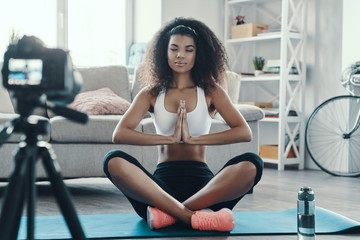 Beautiful young African woman sitting in the yoga position while making social media video