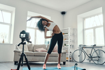Fototapeta na wymiar Full length of flexible young African woman working out while making social media video