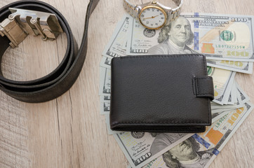 men's wristwatch, men's wallet, belt and dollars on a wooden table. Close-up. Personal belongings of a business man.