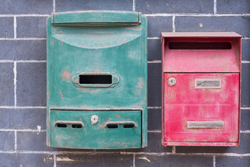 A green and a red old mailbox on a brick wall