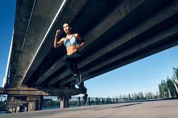 Fototapeta na wymiar Sporty woman running outdoors under city bridge