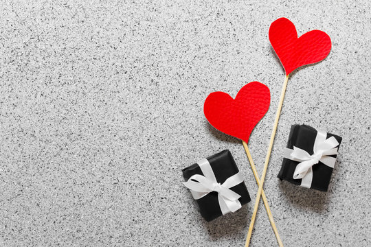Valentine day celebration greeting card with two red hearts on wooden sticks and two little presents with white bows on stone texture background. - Powered by Adobe