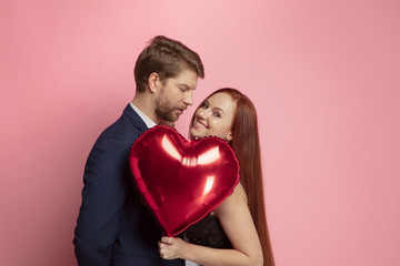 Fototapeta na wymiar Happy holding balloons shaped hearts. Valentine's day celebration, happy caucasian couple on coral background. Concept of human emotions, facial expression, love, relations, romantic holidays.