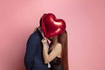 Happy holding balloons shaped hearts. Valentine's day celebration, happy caucasian couple on coral background. Concept of human emotions, facial expression, love, relations, romantic holidays. - obrazy, fototapety, plakaty